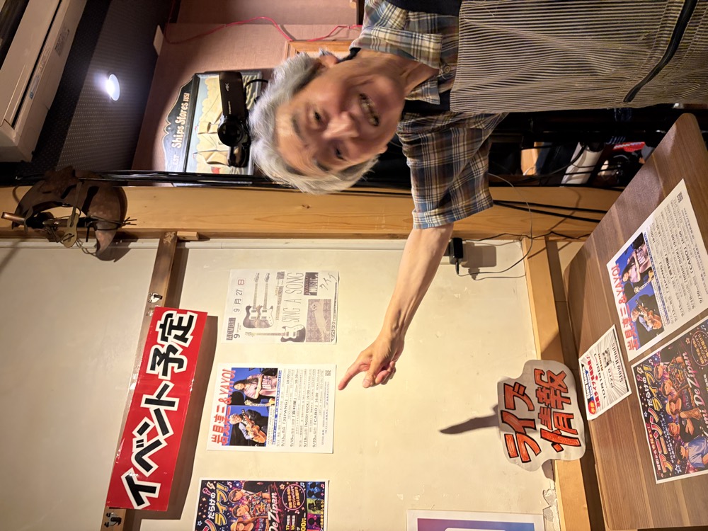 ジパング店内の「イベント予定」コーナーを指差す店長さん